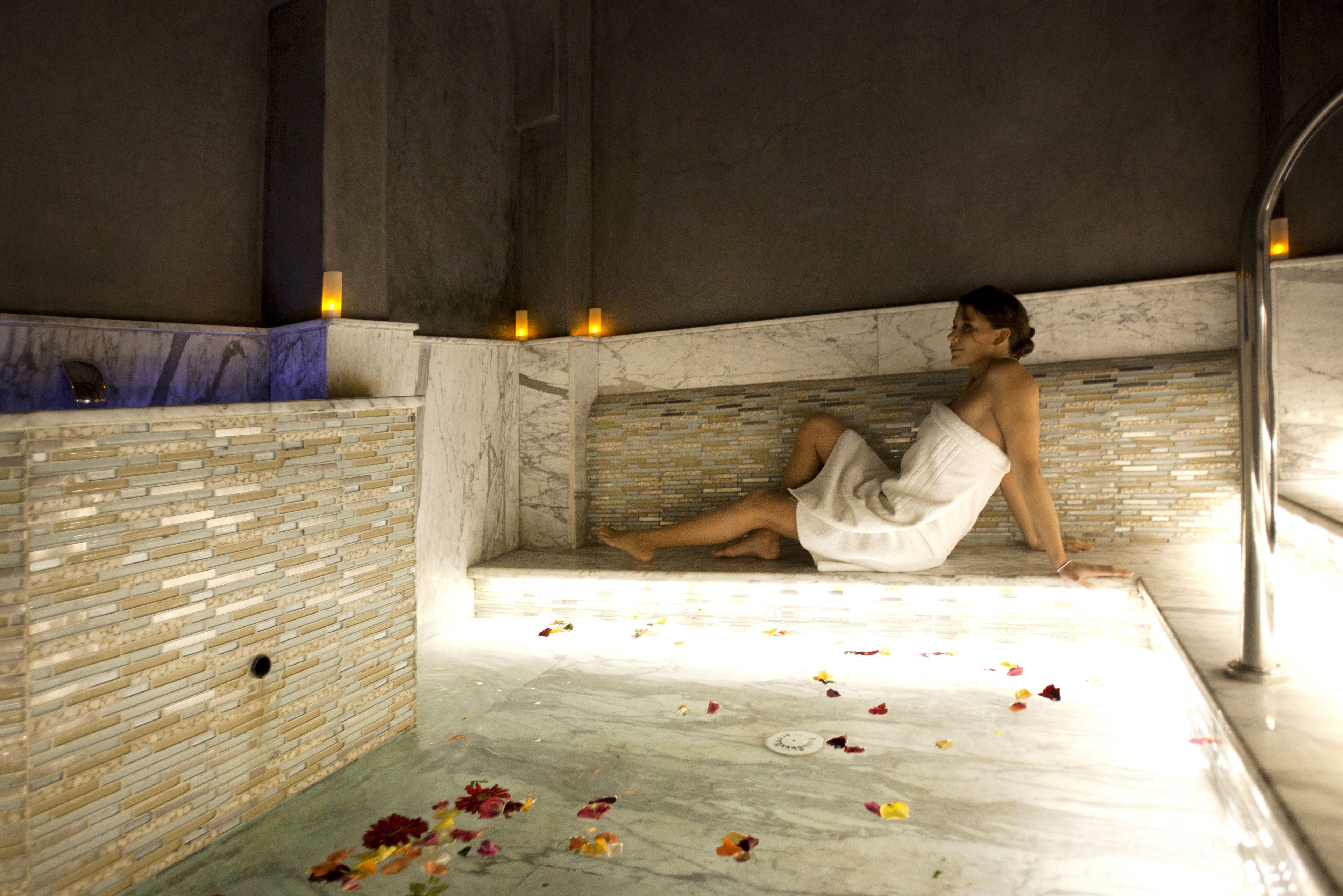 A person sitting in a bathtub with rose petals scattered around.