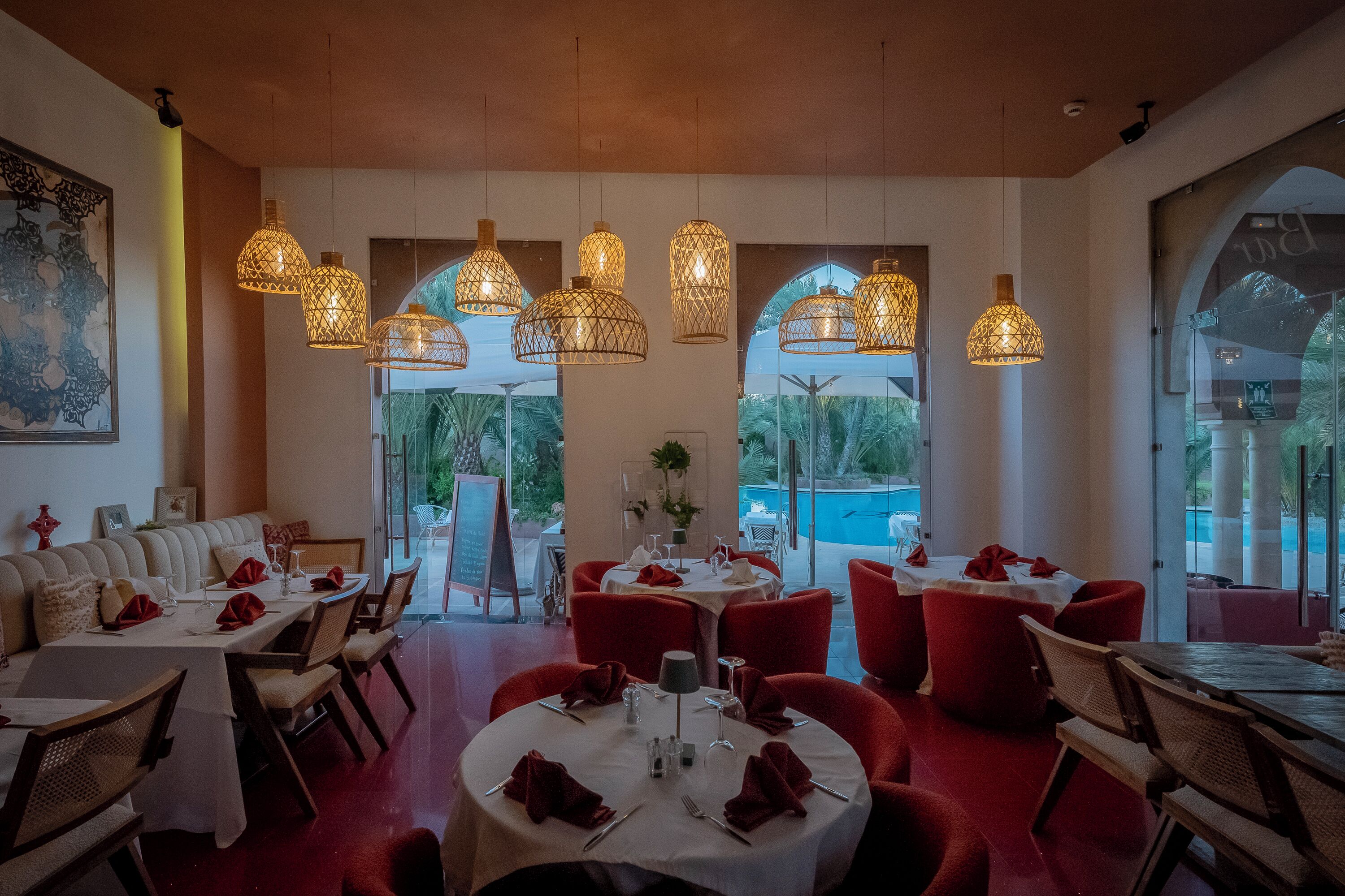 A restaurant with round tables, red chairs, and hanging pendant lights.