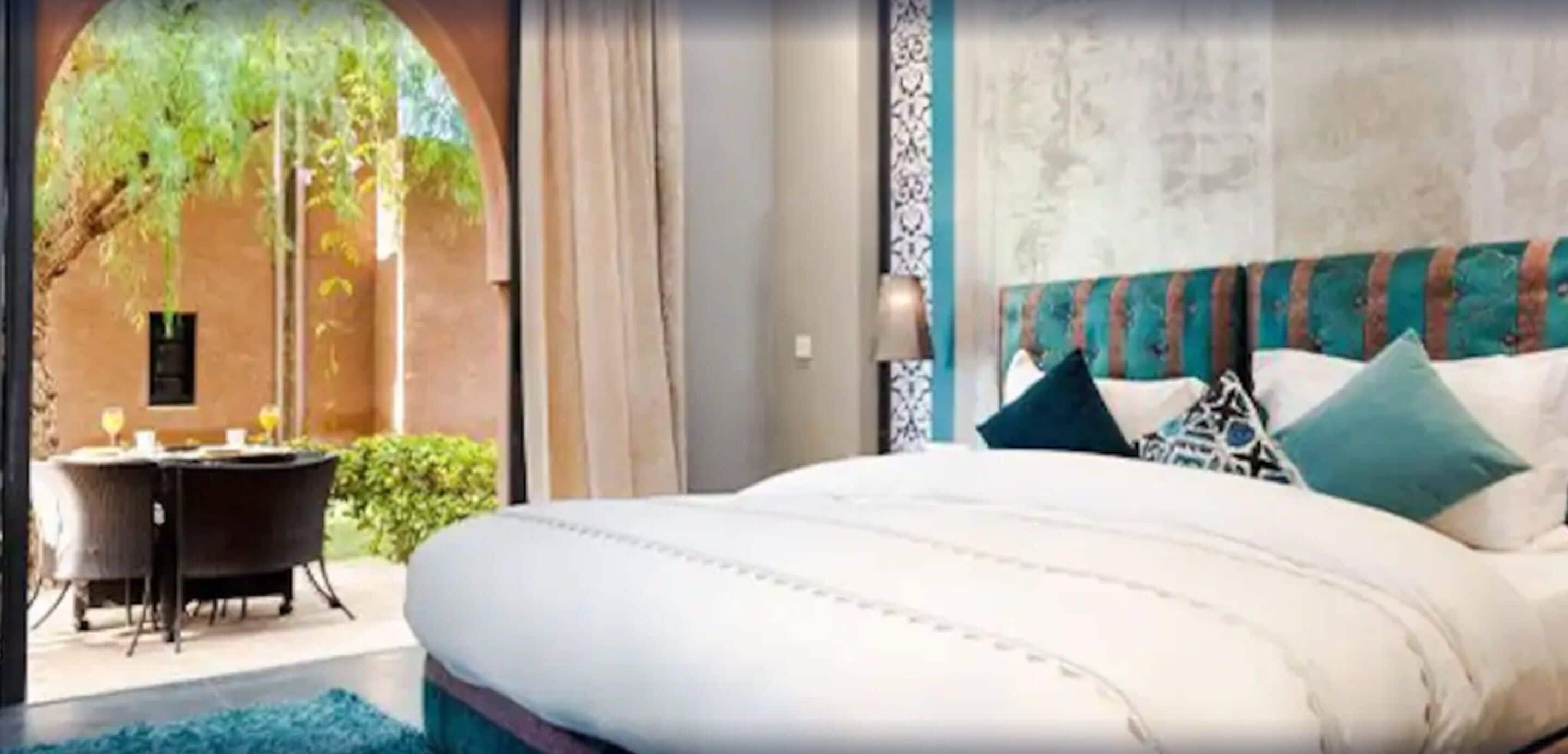 A bedroom with a large bed, a view of greenery outside, and a dining area with a table and chairs.
