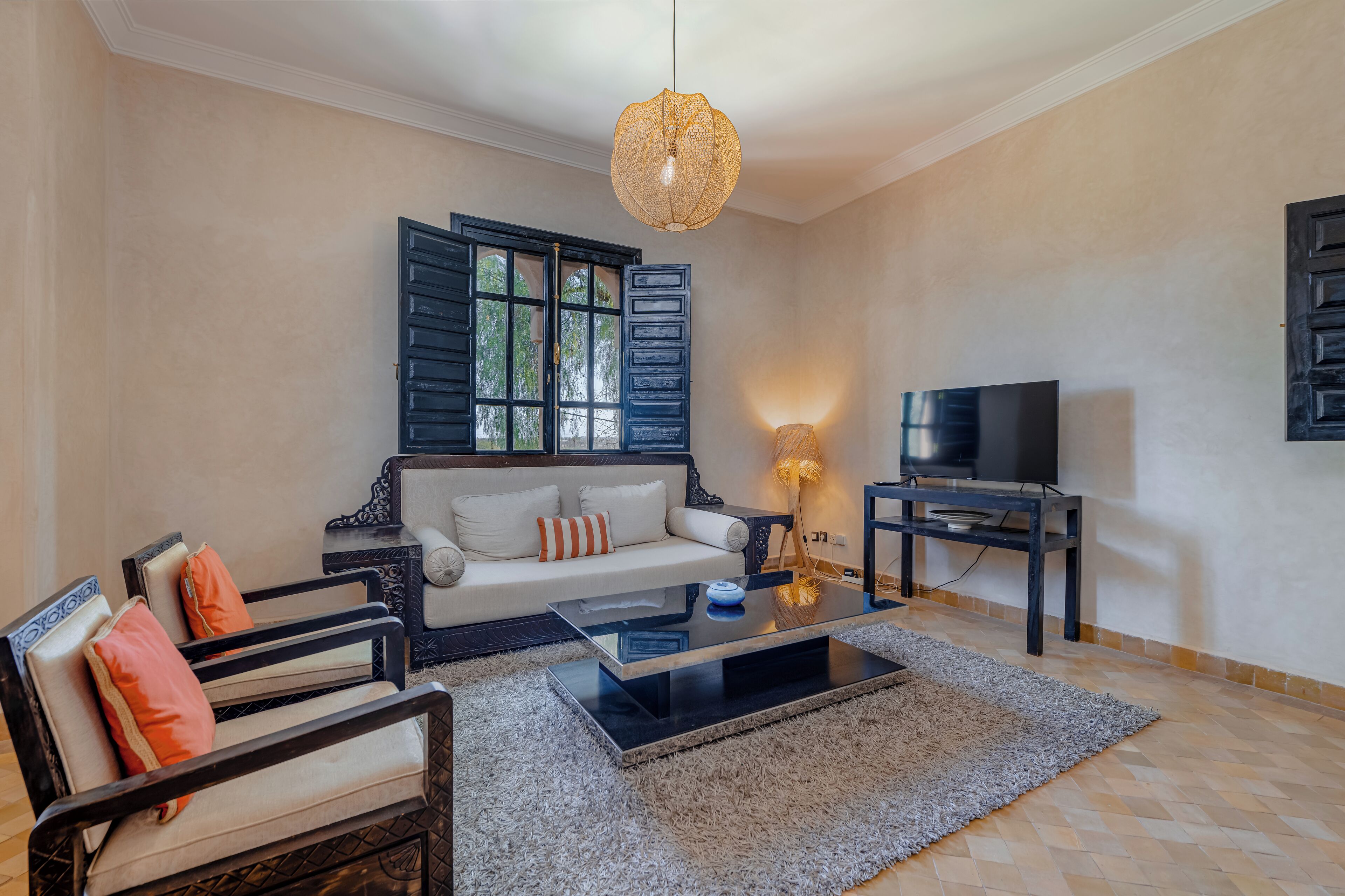 Un salon comprenant un canapé, des fauteuils, une table basse, un téléviseur et un luminaire décoratif.