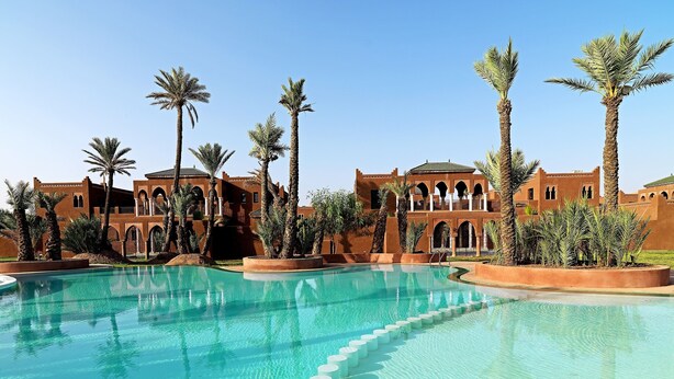 Un complex turístic amb una piscina gran, palmeres i arquitectura tradicional.