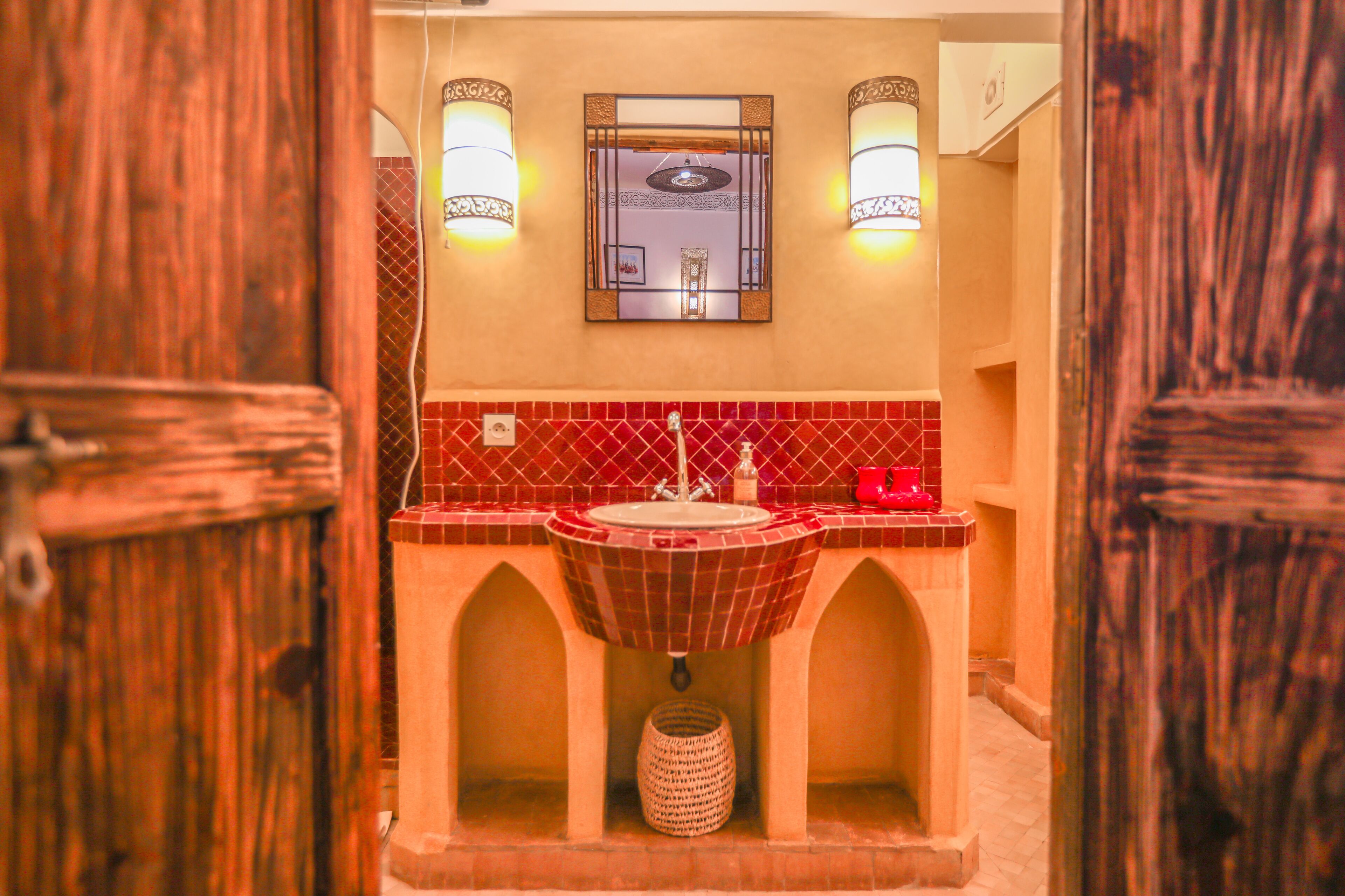 A bathroom with a red-tiled sink, two wall-mounted lights, and a mirror above the sink.