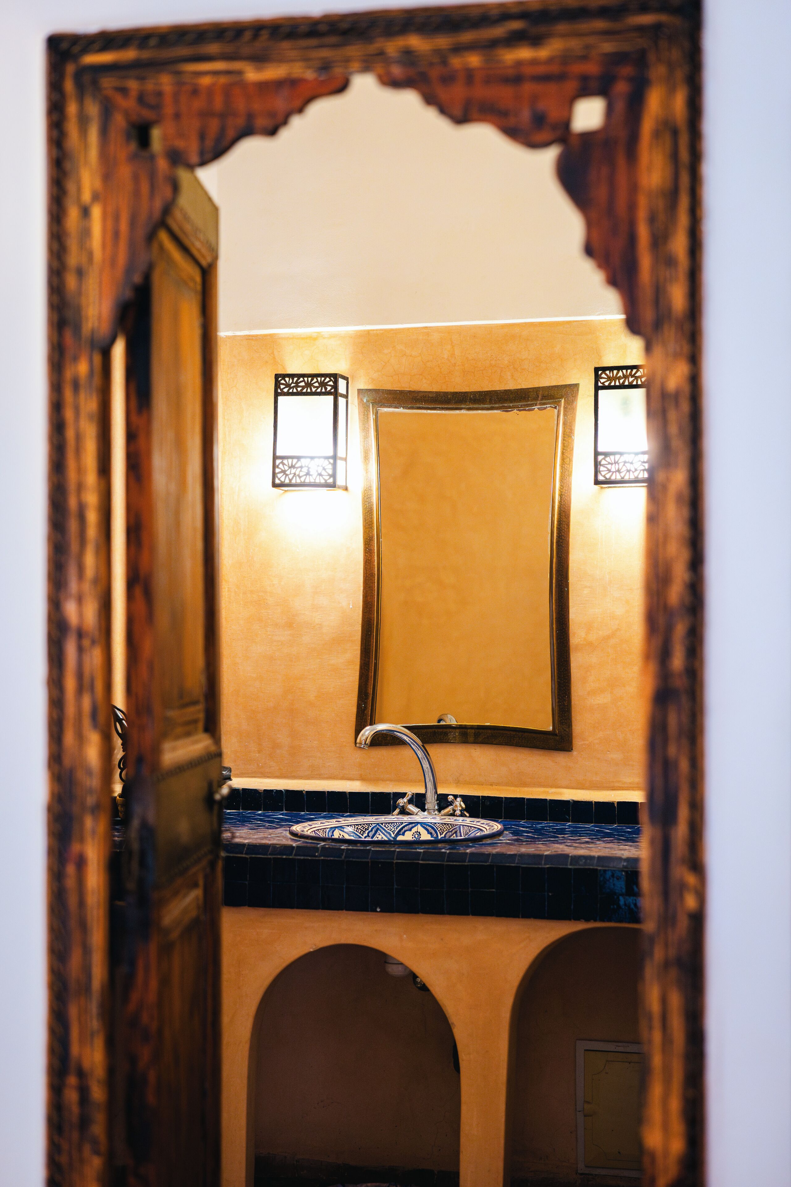 Un baño con espejo de marco de madera, lavabo con encimera azul y dos luces empotradas.