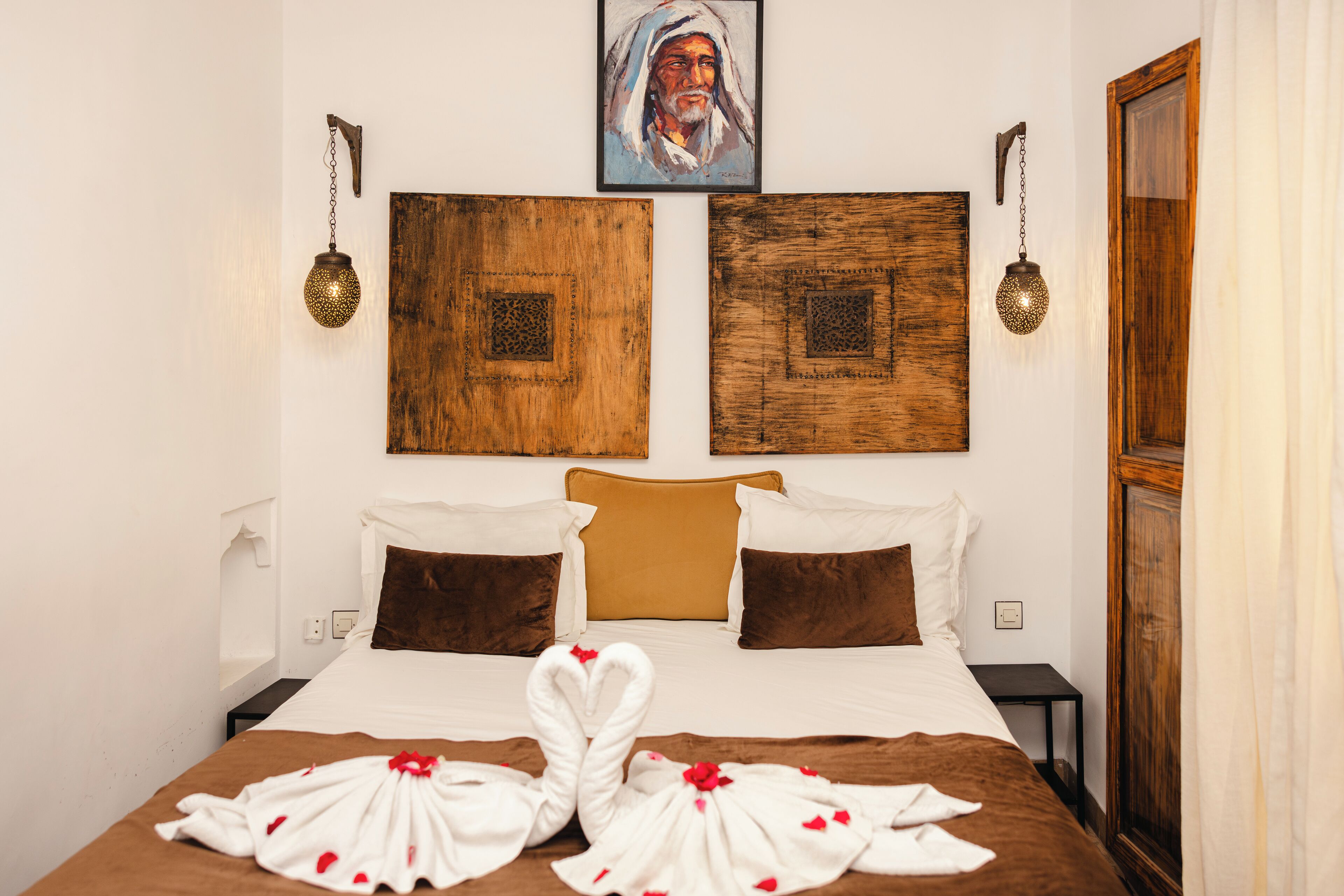 A hotel room with a large bed, two wall-mounted lamps, a wooden headboard, and a painting above the bed.