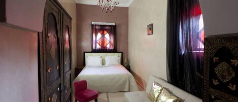 A bedroom with a bed, a red chair, a white sofa, a chandelier, and a large window with curtains.