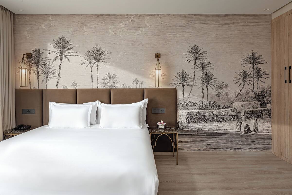 Un dormitorio con una cama grande, cabecera, mesita de noche, un mural en la pared y suelo de madera.