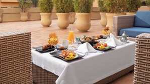 Zona de menjador al terrat amb barra de buffet, plantes en testos i vista d'un edifici d'àmbit urbà amb balcons.