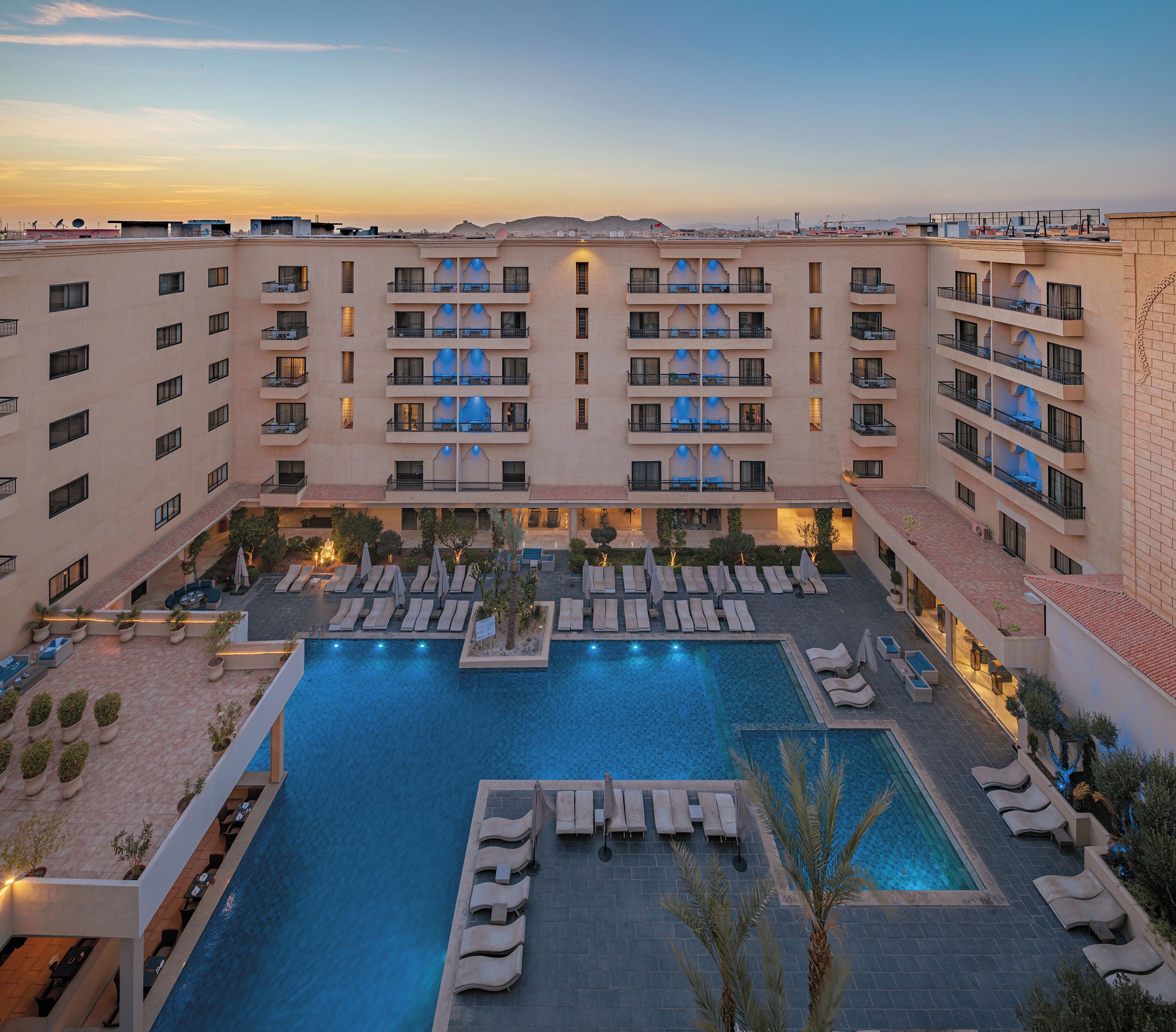 A hotel with multiple balconies, a central swimming pool, and outdoor seating areas.