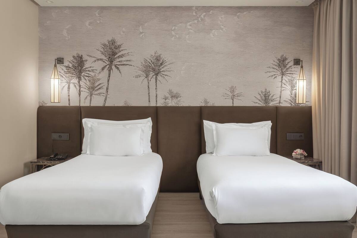 Habitación de hotel con dos camas, un gran mural de palmeras en la pared y dos lámparas de noche.