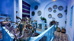 Habitación con paredes azules, una escalera, plantas en macetas y platos decorativos en las paredes.