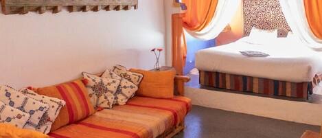 Una habitación acogedora con un sofá de madera, una cama con cortinas naranjas y una alfombra estampada.