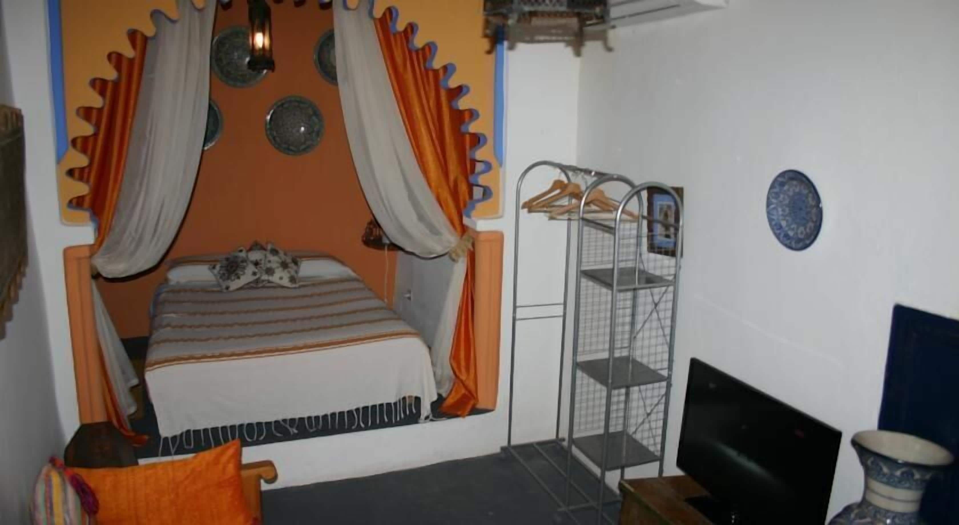 A bedroom with a bed, curtains, a metal shelf, a television, and a vase.