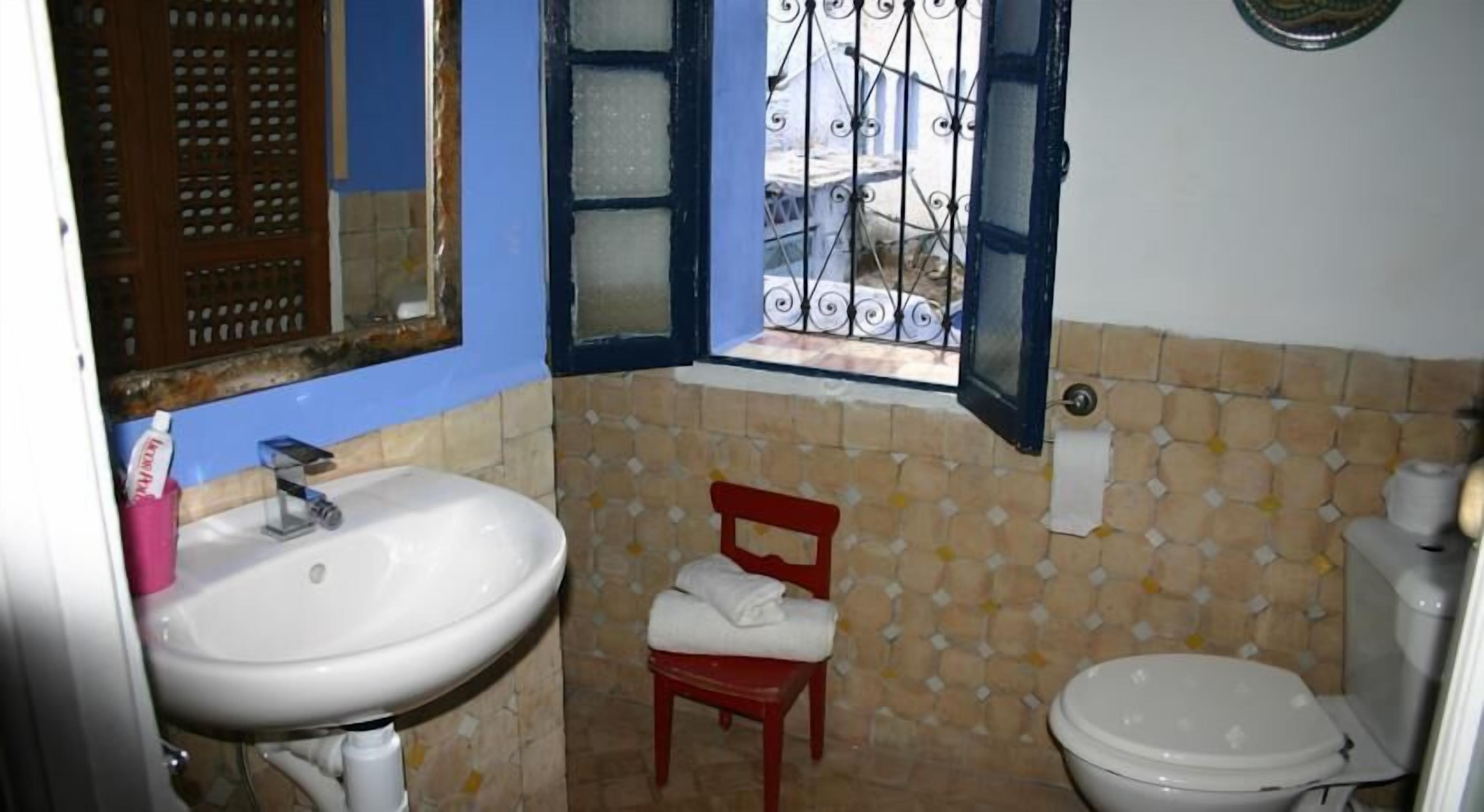 Un baño pequeño con un lavamanos blanco, una silla roja y un inodoro.