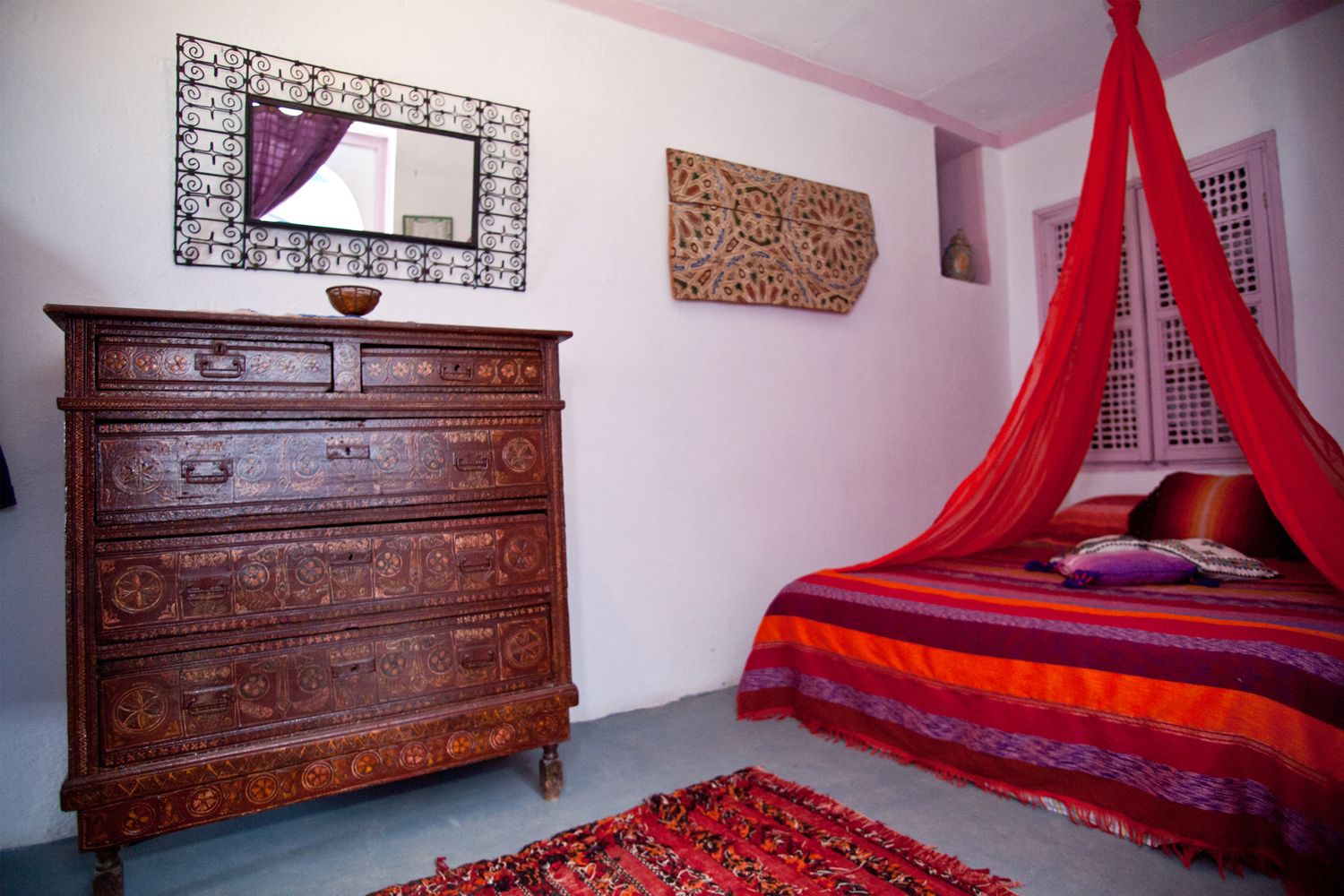 Een slaapkamer met een houten dressoir, een bed met rode hemel en een decoratief wandkunstwerk.