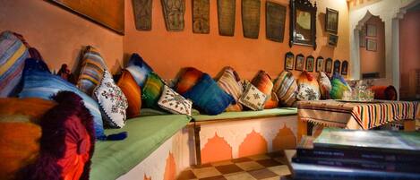 Una habitación tradicional con un sofá decorado con cojines de colores, piso a cuadros y una mesa con libros.