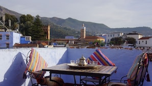 Terraza en la azotea con una mesa lista para cenar, con vistas a un paisaje montañoso y edificios tradicionales.