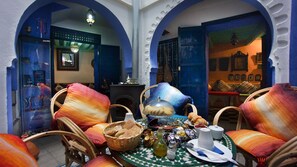 A traditional Moroccan interior with a dining area featuring wicker chairs, a table set with bread, olives, and a bottle of olive oil. - Hotel Casa Miguel (Chefchaouen)