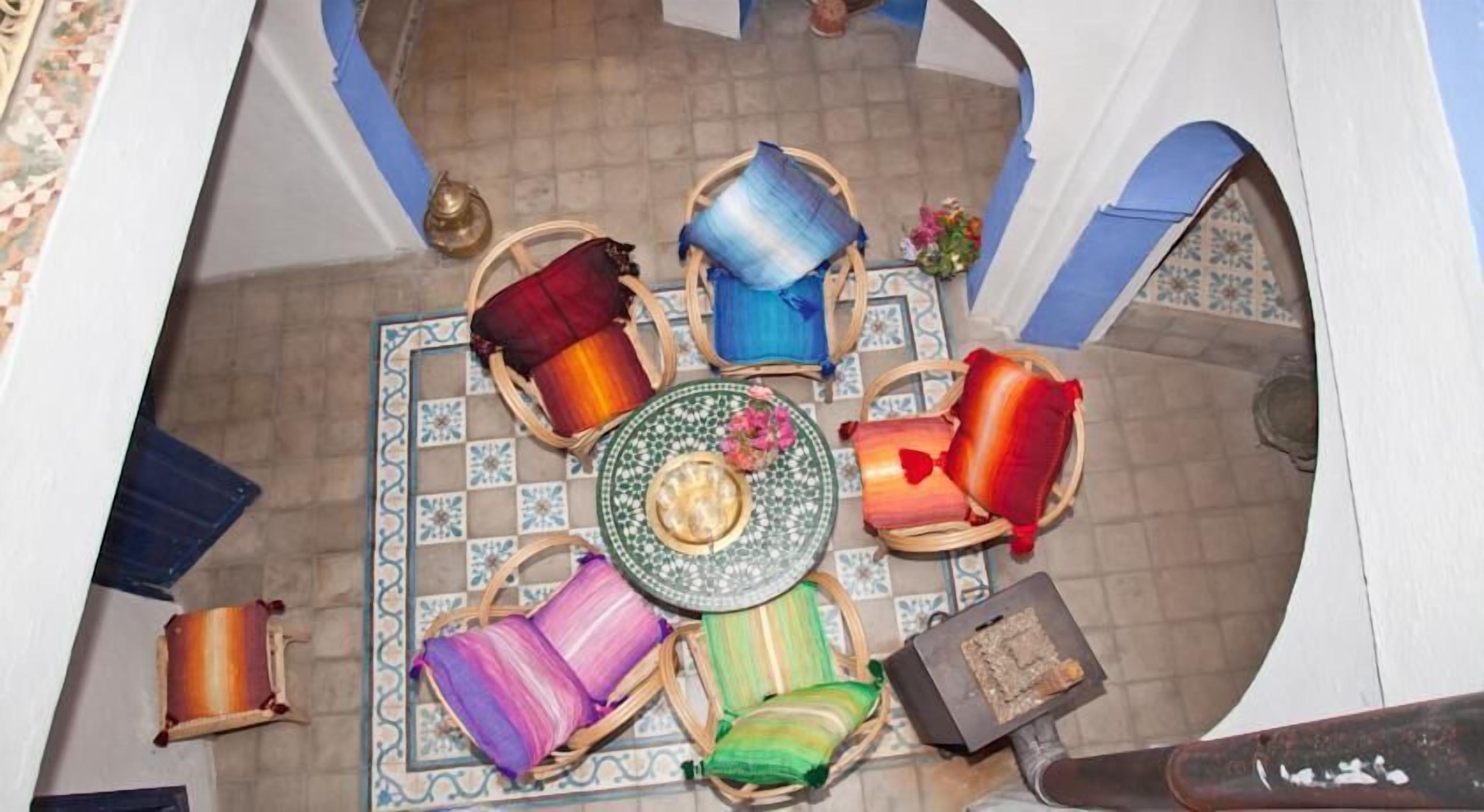 A Moroccan riad with a tiled floor, a central coffee table, and colorful cushions arranged around it.