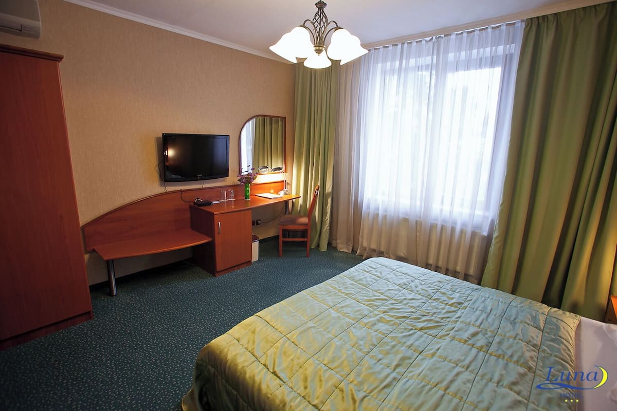 Une chambre d’hôtel avec un lit, un bureau et une chaise, une télévision et une fenêtre avec des rideaux.
