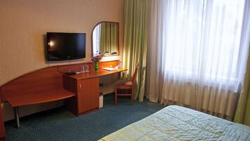 Ein Hotelzimmer mit Bett, Schreibtisch, Stuhl, Fernseher und einem Fenster mit Vorhängen.
