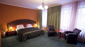 Una habitación de hotel con una cama grande, un escritorio, dos sillas, una mesita de noche y un florero con flores.
