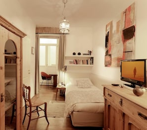 A bedroom with a bed, a desk, a chair, a television, and a bookshelf.