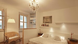 Une chambre à coucher avec un grand lit, une chaise, une table de chevet, une lampe, un lustre et un tableau au mur.