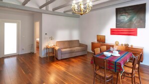 Une pièce spacieuse avec un plancher en bois, un canapé, une table à manger avec des chaises, un lustre et un tableau accroché au mur.