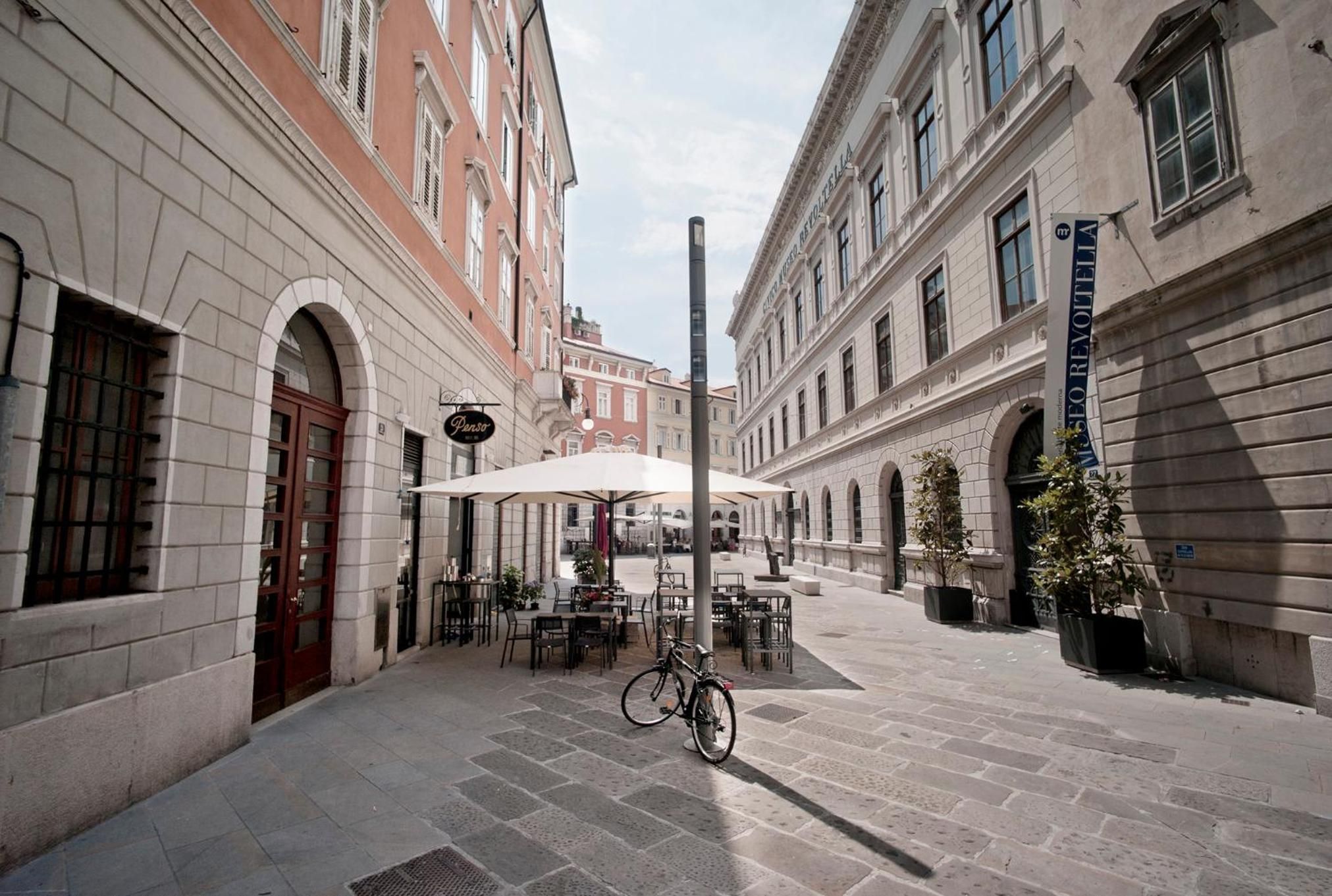 Un espace café en plein air avec des tables et des chaises, un vélo et une vue sur la rue avec des bâtiments.