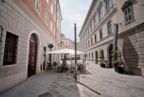 An outdoor café area with tables and chairs, a bicycle, and a street view with buildings.