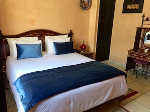A bed with white and blue bedding, a wooden headboard, and a nightstand with a red lamp. - Essaouira Wind Palace (Essaouira)
