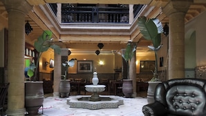 A spacious lobby with a central fountain, large potted plants, and a leather armchair. - Essaouira Wind Palace (Essaouira)