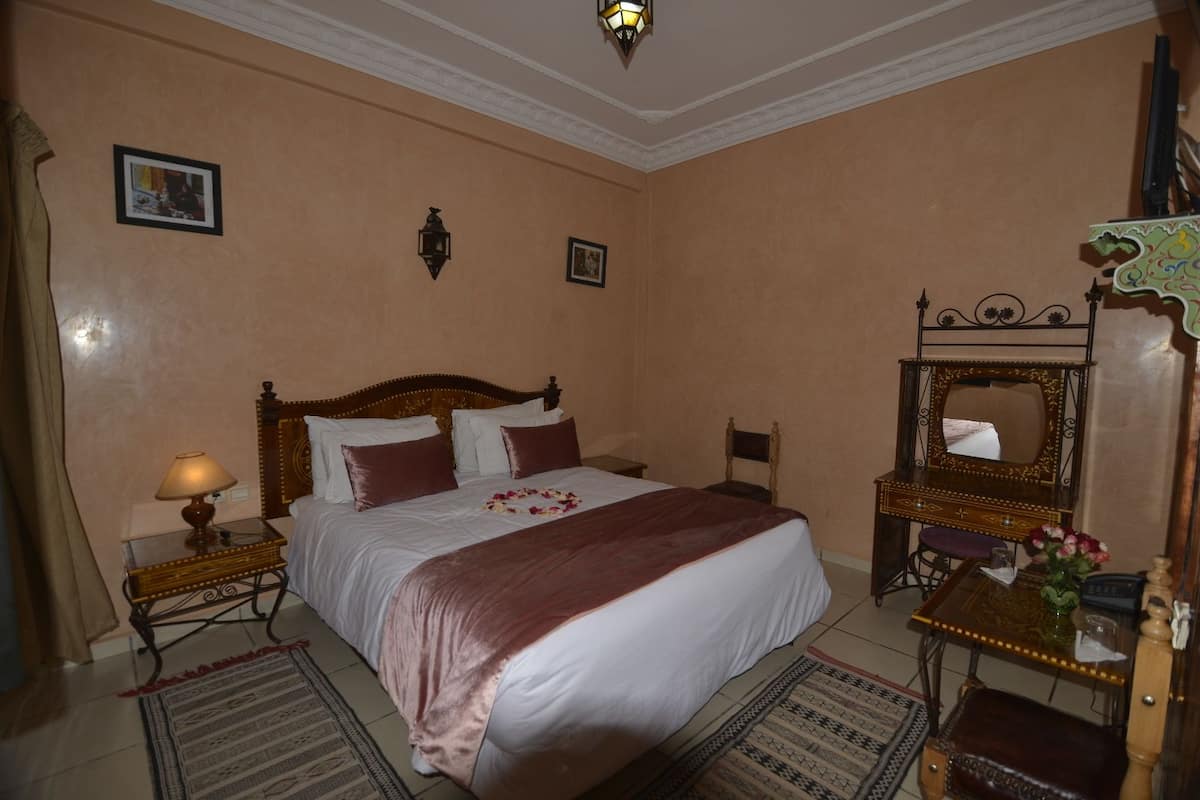 A neatly arranged bedroom with a large bed, bedside tables, a mirror, and a decorative lamp.