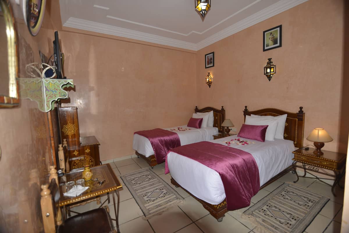 A hotel room with two beds, a wooden desk, a chair, a mirror, and a lamp.