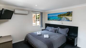 Un dormitorio con cama, televisor, aire acondicionado, un cuadro de una playa y una ventana.