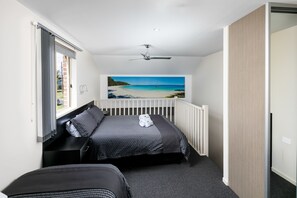 Une chambre à coucher avec un lit, une vue sur la plage, un ventilateur de plafond et une fenêtre avec des rideaux.