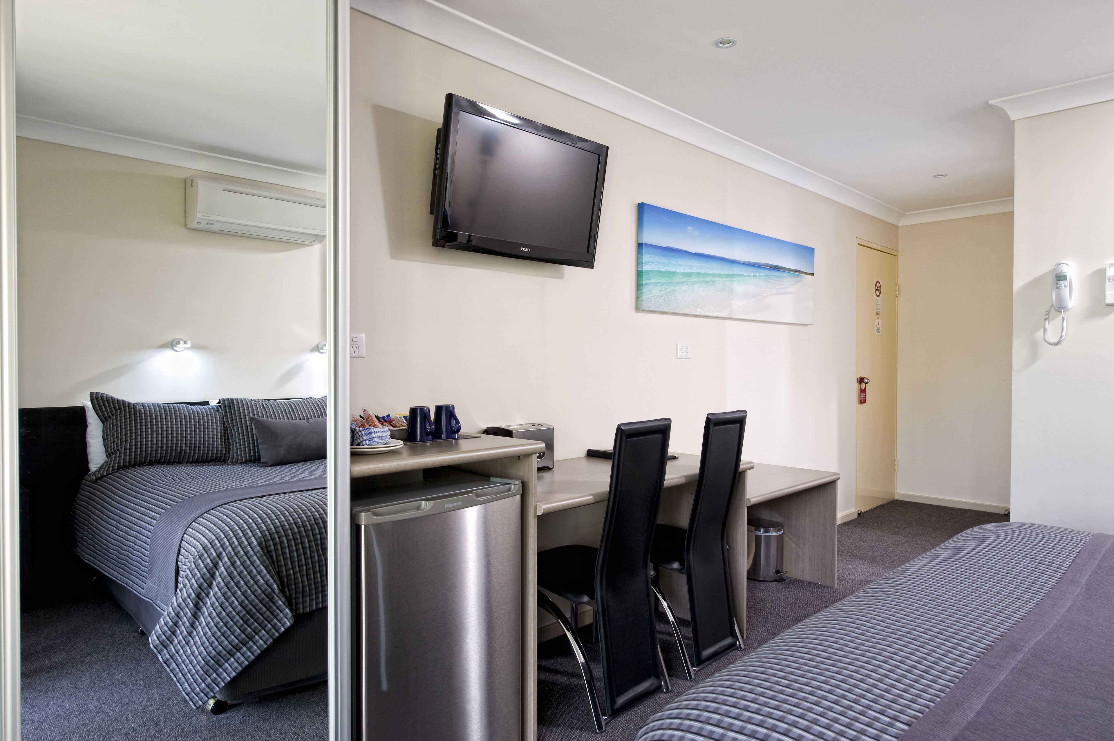 A hotel room with a bed, a desk with a computer, a TV, and a painting on the wall.