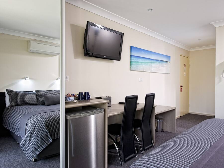 A hotel room with a bed, a desk with a computer, a TV, and a painting on the wall.