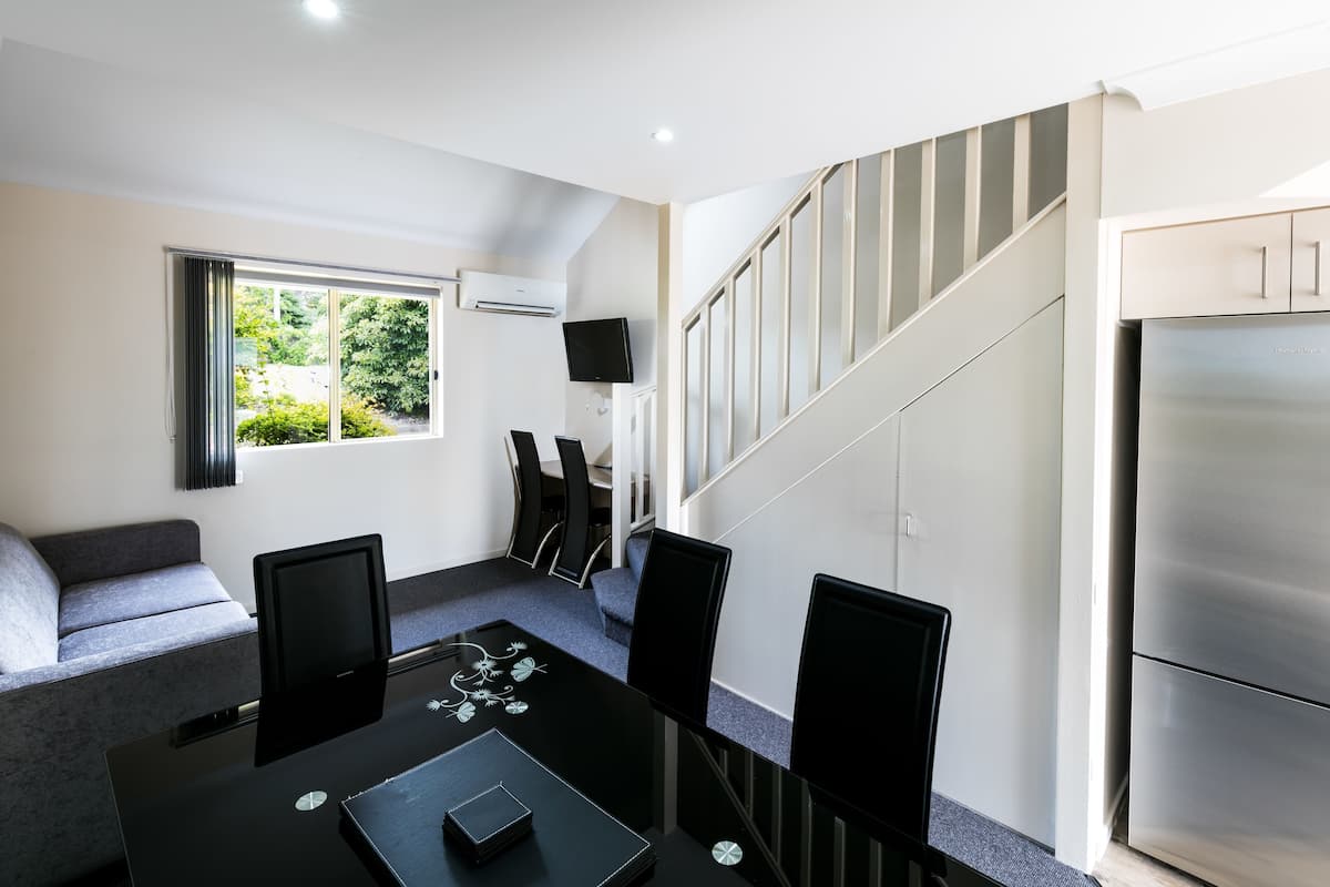 A modern living room with a sofa, a dining table with chairs, a flat-screen TV, and a staircase leading to a kitchen area.