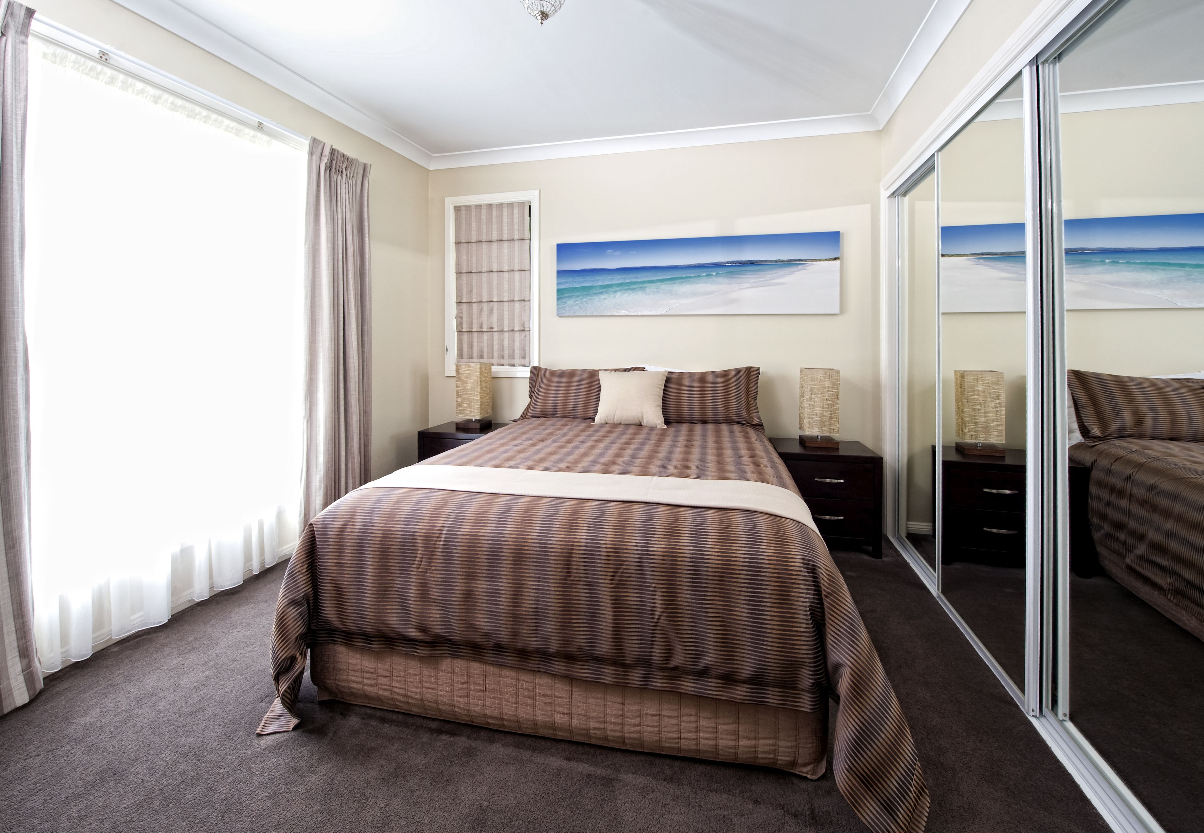 A hotel room with a large bed, a window with curtains, a painting of a beach, and a sliding glass door.