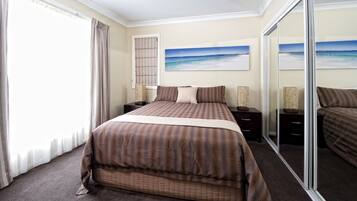 Una habitación de hotel con una cama grande, una ventana con cortinas, un cuadro de una playa y un ventanal corredero.