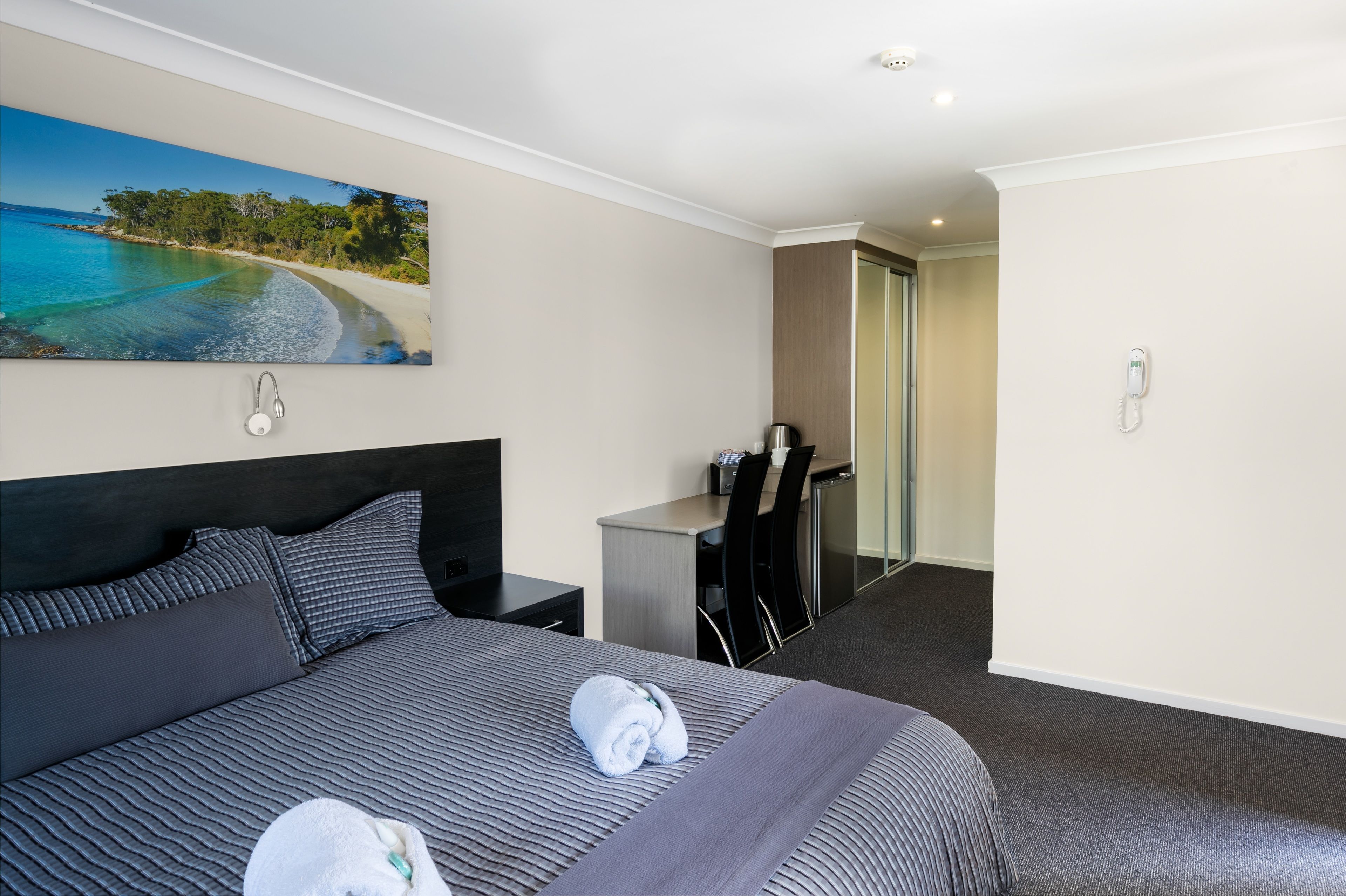 A hotel room with a large bed, a desk, a chair, and a painting of a beach scene.