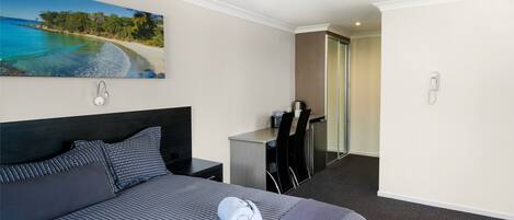 A hotel room with a large bed, a desk, a chair, and a painting of a beach scene.