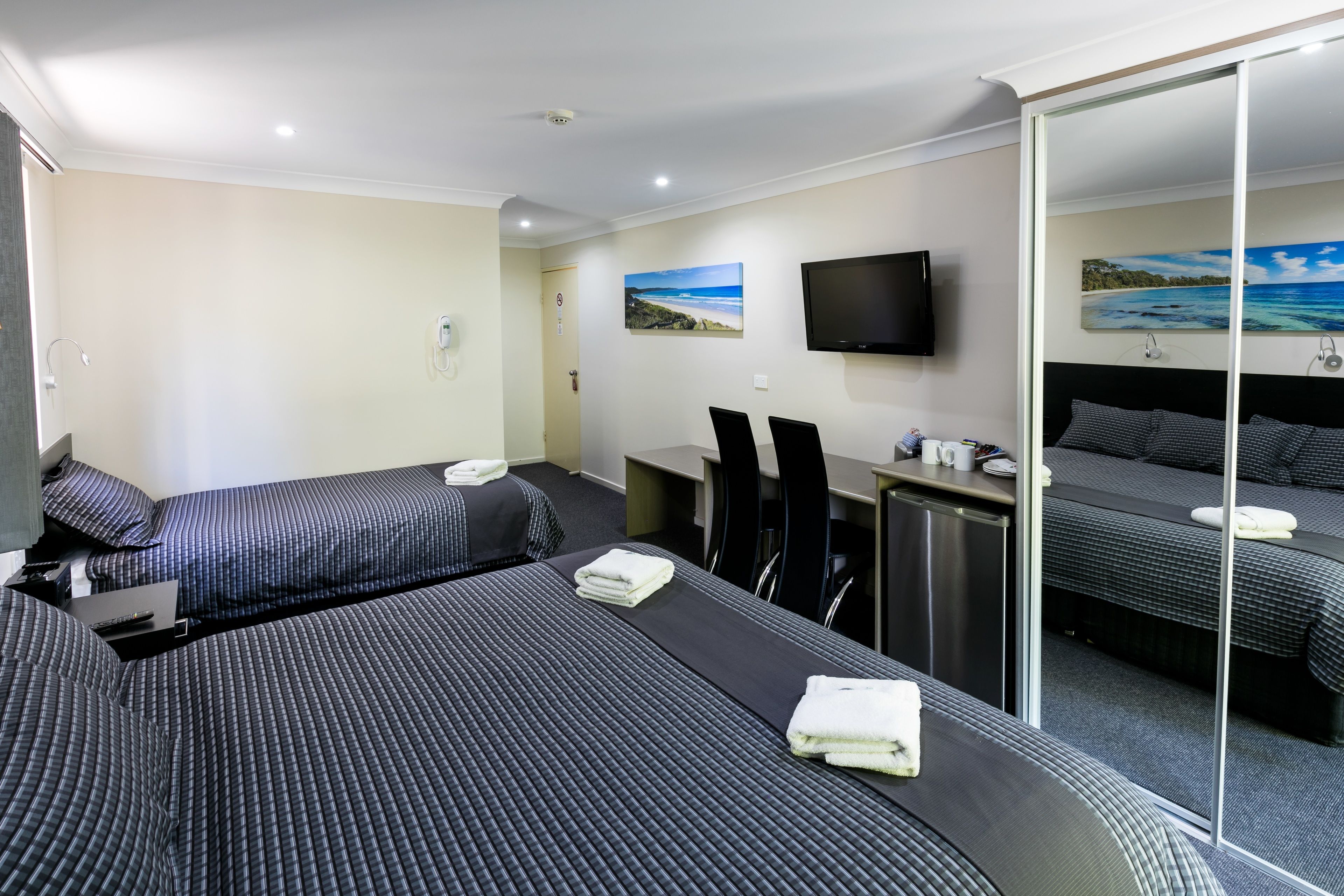 Ein Hotelzimmer mit zwei Betten, einem Schreibtisch, einem Fernseher und einem Strandbild.