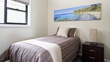 A bedroom with a bed, a nightstand, a window, and a beach scene painting on the wall.