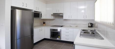 A modern kitchen with white cabinets, stainless steel appliances, a built-in oven, and a sink.