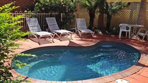 A swimming pool with a brick border, surrounded by white lounge chairs and a brick patio. - Dolphin Shores (Vincentia)