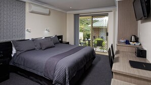 A modern hotel room with a large bed, a desk with a flat-screen TV, a coffee maker, and a sliding glass door leading to a balcony. - Dolphin Shores (Vincentia)