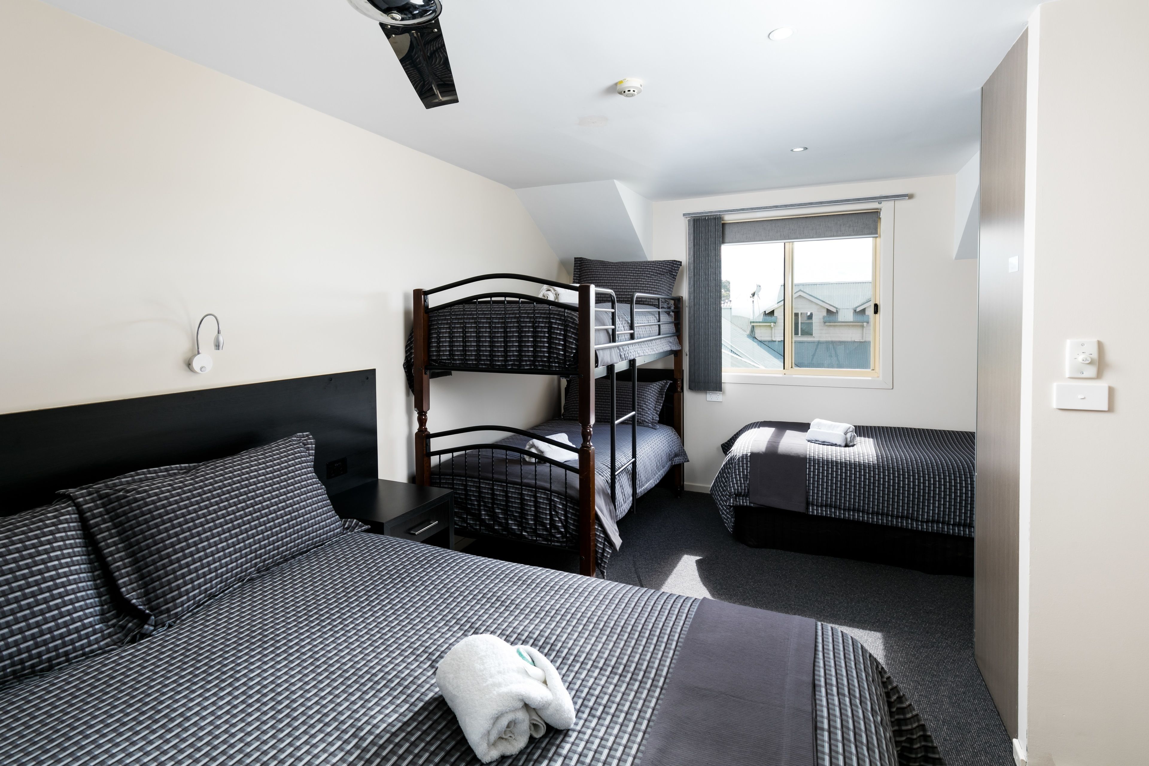 A hotel room with a bunk bed, a single bed, and a window with a view.
