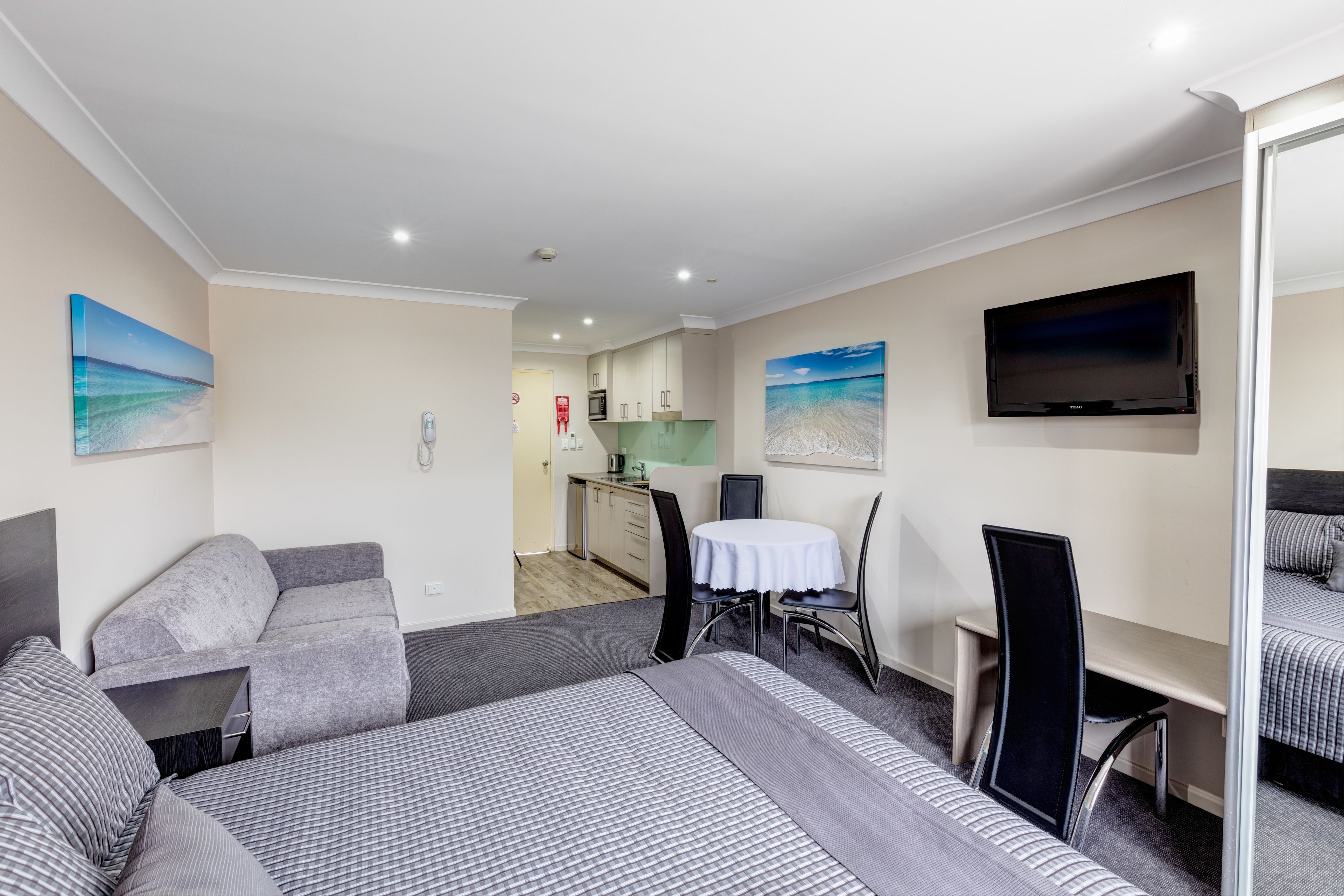 Een hotelkamer met een groot bed, een bureau, een stoel, een televisie en een kitchenette op de achtergrond.
